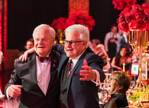 Two older gentlemen in formal dress with their arms around each others' shoulders.